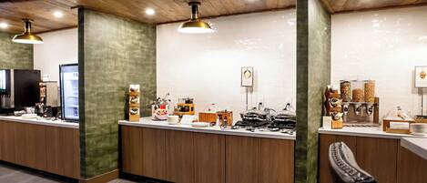 Una cocina moderna con armarios de madera, una encimera con diversos electrodomésticos e iluminación colgante.