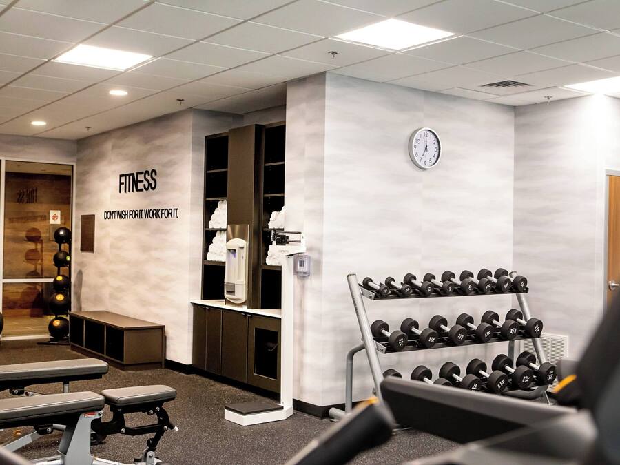 A gym with exercise equipment, dumbbells, and a wall clock.