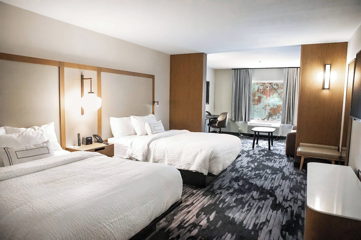 A hotel room with two beds, a desk, a chair, and a large window with curtains.