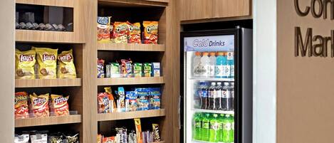 A vending machine stocked with snacks and cold drinks, surrounded by shelves of packaged goods.