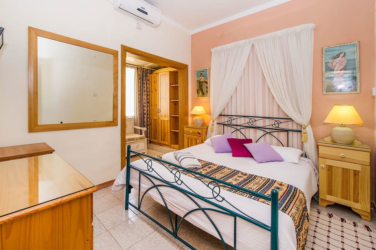 A bedroom with a bed, bedside tables, a wardrobe, a mirror, and a window with curtains.