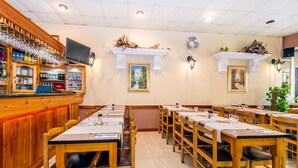 A restaurant with wooden tables and chairs, a bar area with shelves of bottles and glasses, and wall-mounted artwork. - Lantern Guest House (Zebbug)