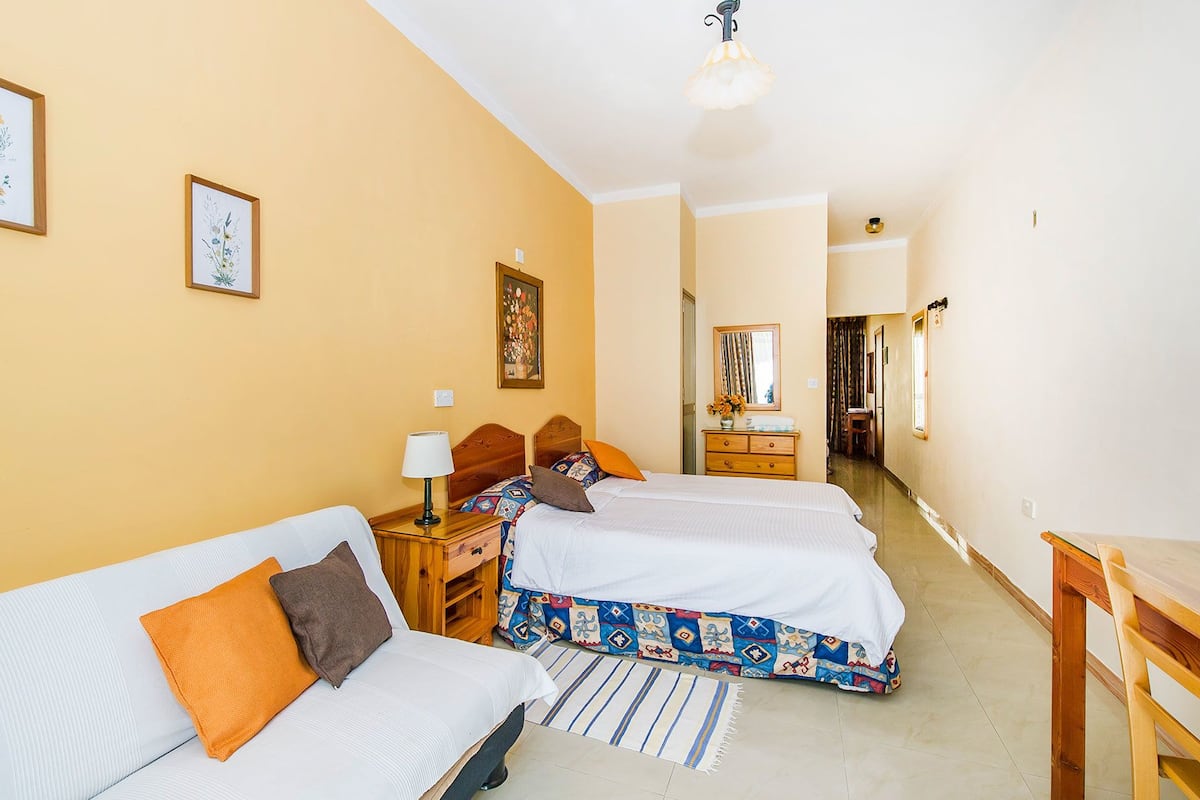 A hotel room with two beds, a desk, a chair, a lamp, and a mirror.