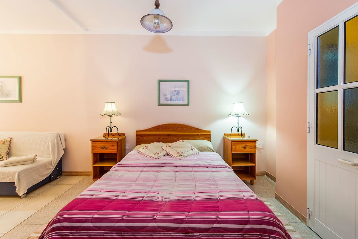 A bedroom with a bed, bedside tables, a nightstand, a chair, and a window with frosted glass.