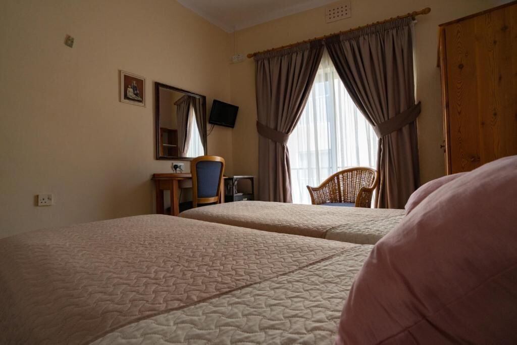 A hotel room with two beds, a desk with a chair, a television, and a large window with curtains.