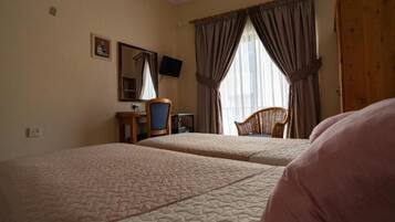 A hotel room with two beds, a desk with a chair, a television, and a large window with curtains.