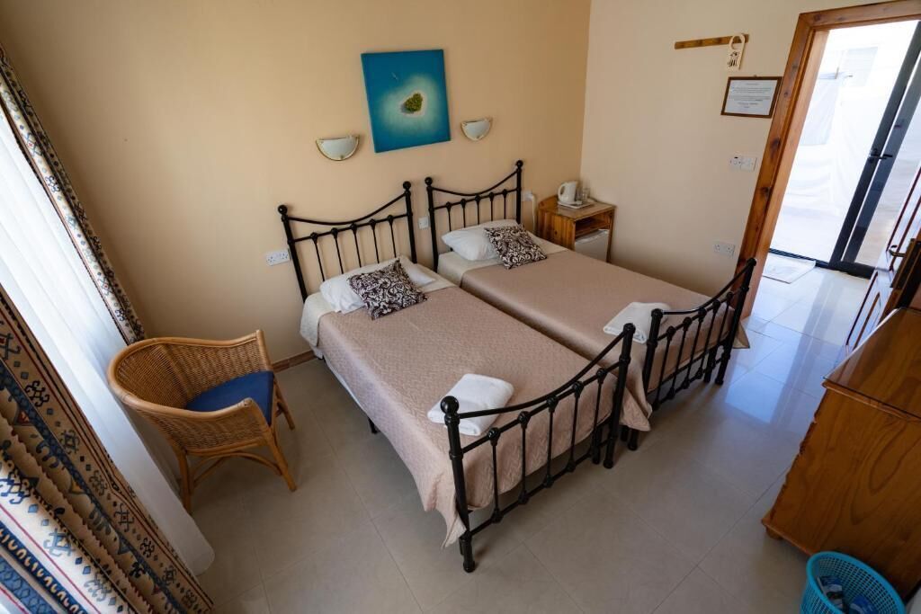 A room with two beds, a chair, a small table, and a painting on the wall.