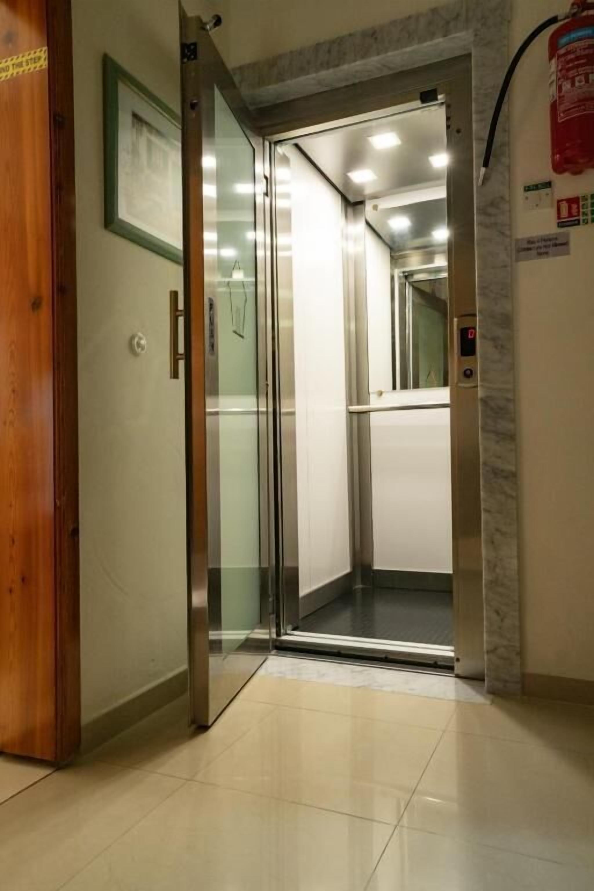 A hotel elevator with a wooden door, a framed picture on the wall, and a fire extinguisher on the wall.