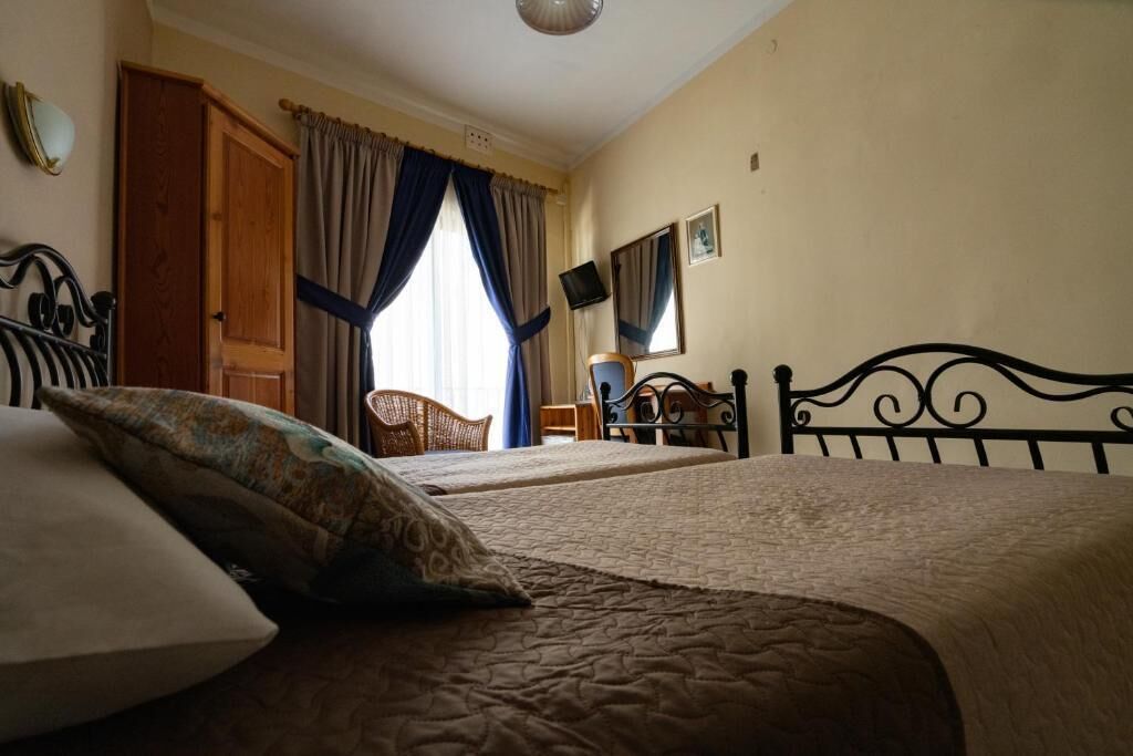 A bedroom with two beds, a wooden door, and a window with curtains.