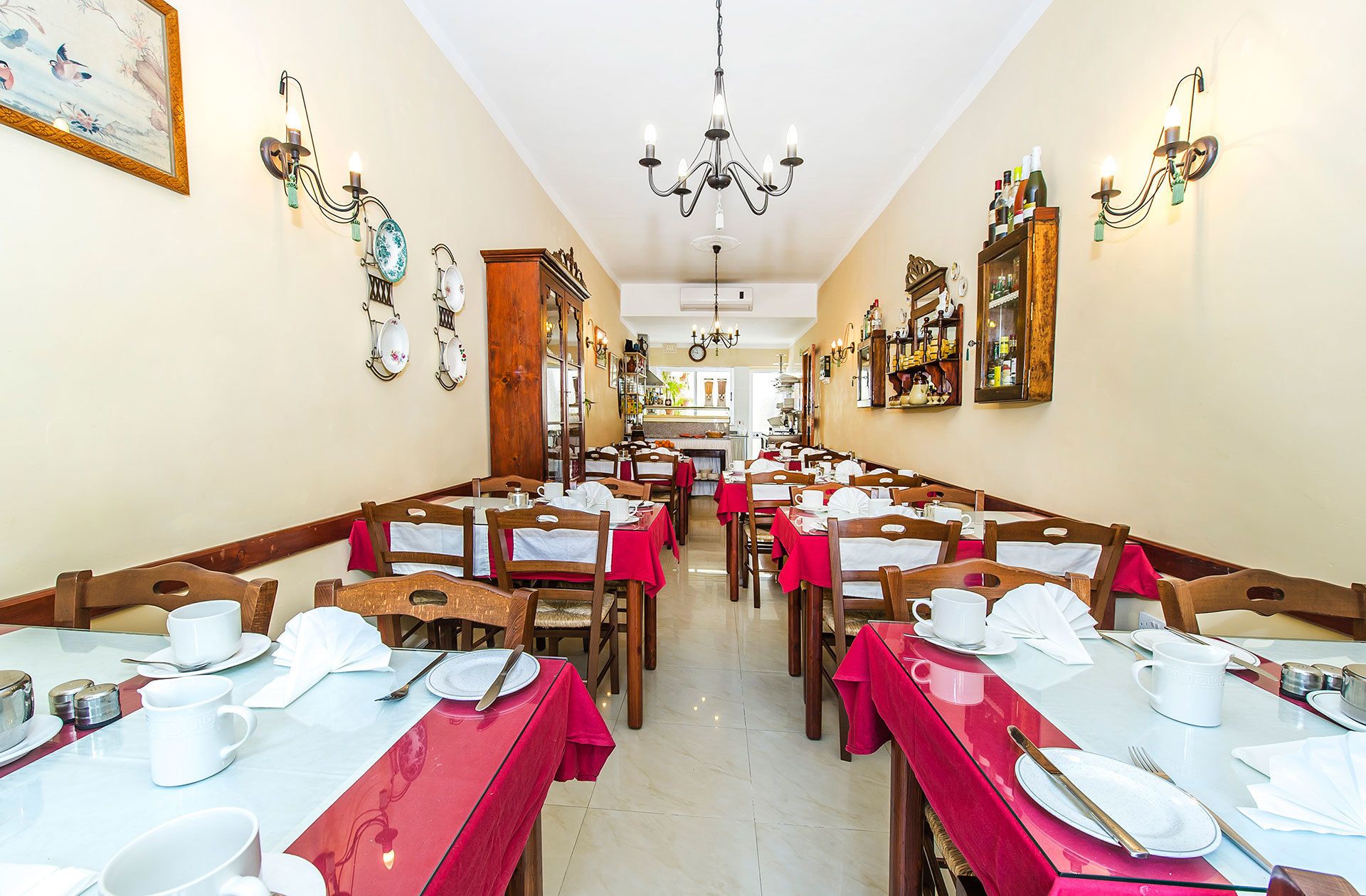 A restaurant with long communal tables, red tablecloths, and a chandelier.