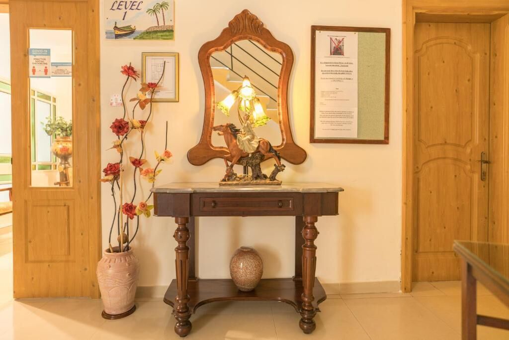 Una puerta de madera, un espejo, un florero con flores y un certificado en un marco en la pared.