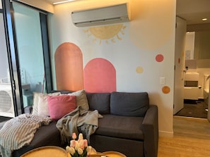 A modern living room with a grey sofa, a pink pillow, a grey throw blanket, and a vase of tulips. - Free Tram Zone 2BR Apt near QV Market & RMIT (Melbourne)