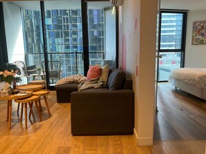 A modern living room with a sofa, a small round table, and a chair. There is a large window with a view of buildings outside.