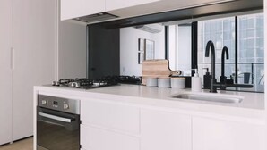 A modern kitchen with a gas stove, oven, white cabinetry, a wooden cutting board, and a black faucet.