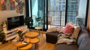 A modern living room with a flat-screen TV, a sofa, a coffee table, and a dining area with chairs.