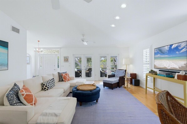 A spacious living room with a large TV, comfortable seating, and a view through glass doors to the outdoors.