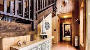 Un intérieur en bois avec une cheminée en pierre, un escalier en bois et un couloir menant à une autre pièce.