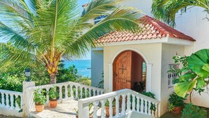 A coastal building with a red-tiled roof, a white balcony with railings, and a wooden door. - Private Ocean View Villa - Chef & Staff Included (Puerto Plata)