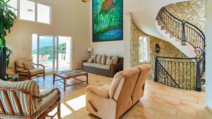 A spacious living area with a large painting, wicker furniture, a beige sofa, and a stone staircase. - Private Ocean View Villa - Chef & Staff Included (Puerto Plata)