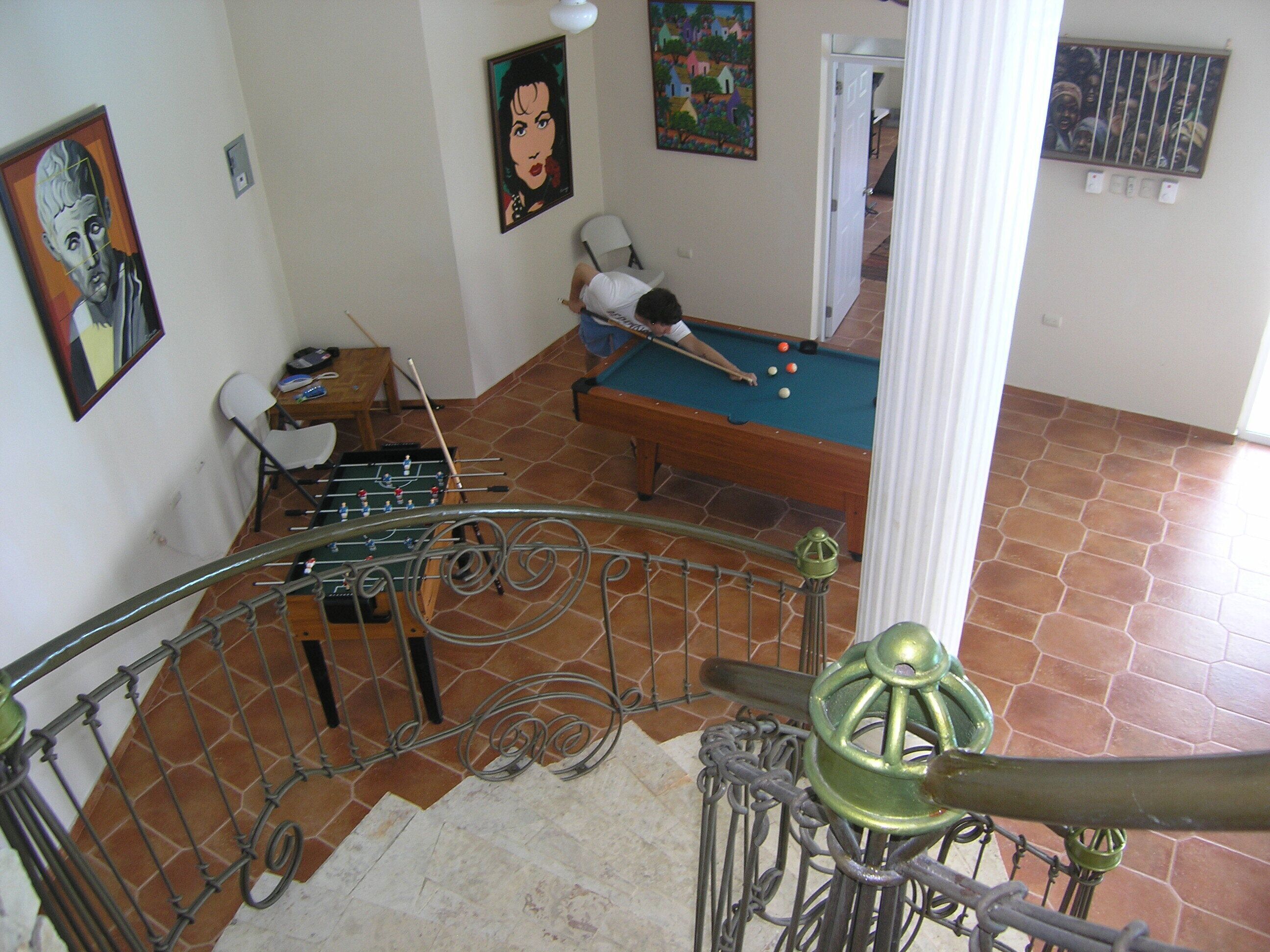 Ein Zimmer mit Billardtisch, Kicker und einer Treppe mit Metallgeländer.