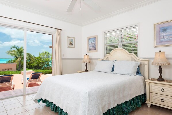 A bedroom with a large bed, two bedside tables with lamps, a window with blinds, and a view of the ocean.