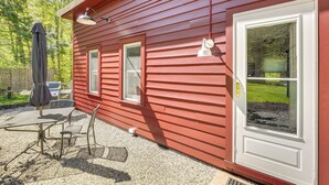 Une maison en bois rouge avec une porte blanche, une fenêtre et une terrasse avec une table et des chaises.