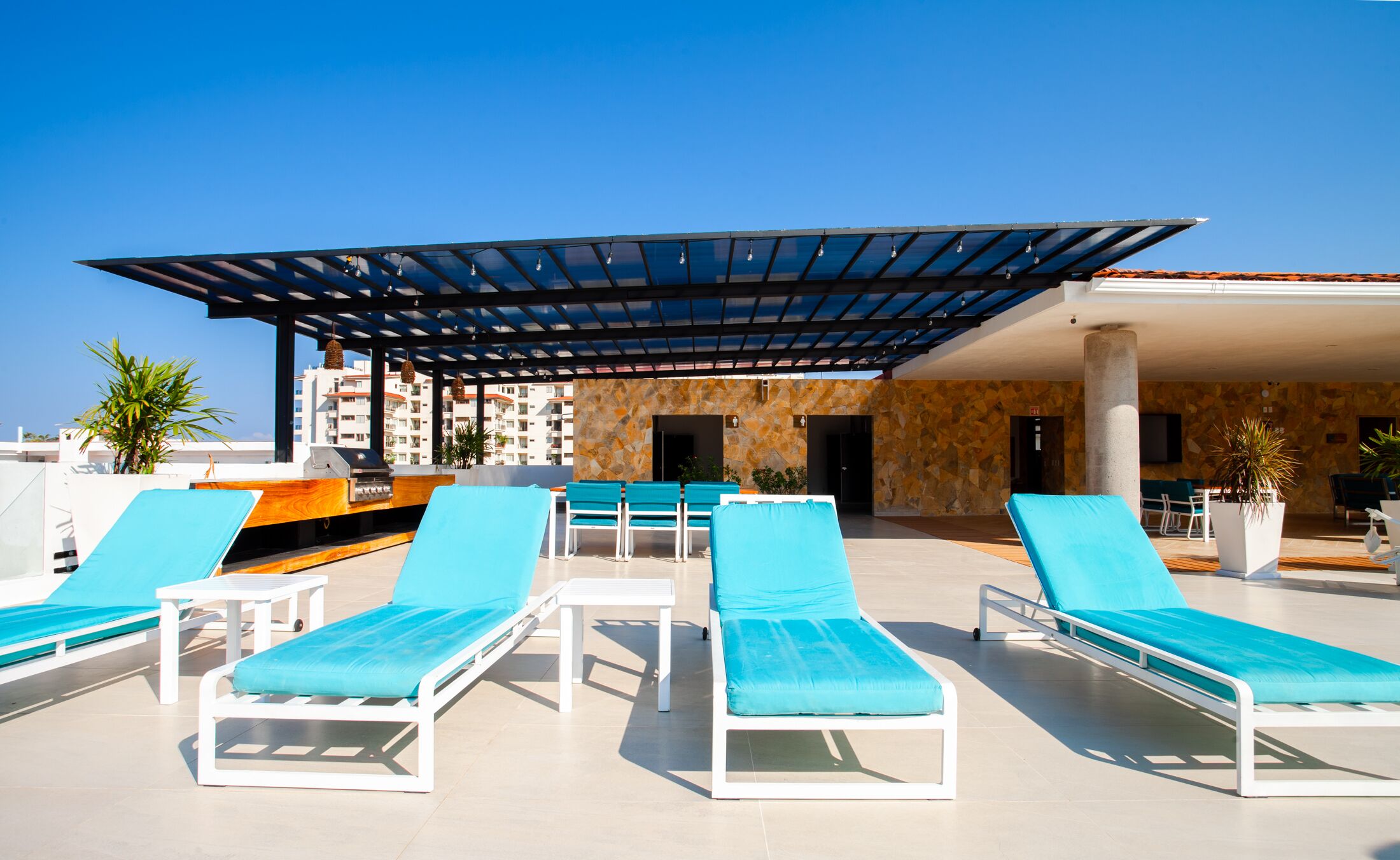 A rooftop pool area with blue lounge chairs, a barbecue grill, and a covered seating area.