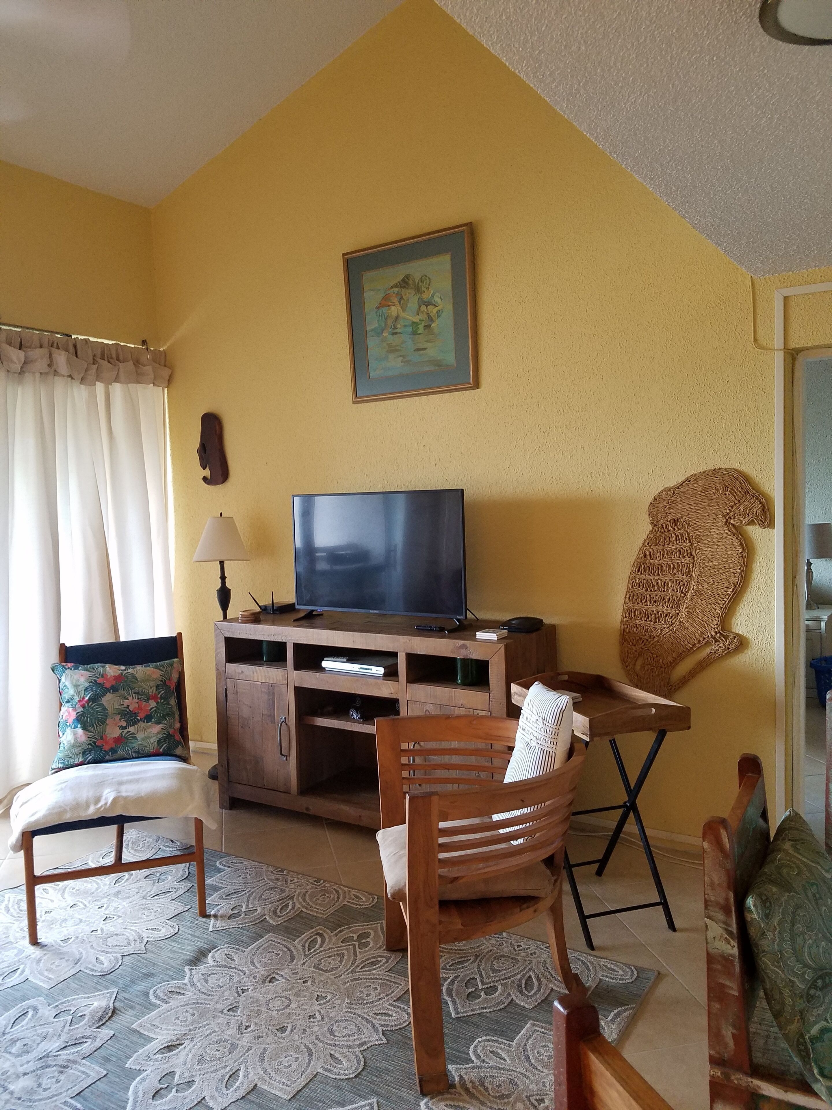 A living room with a television on a wooden cabinet, a chair with a cushion, a patterned rug, and a painting on the wall.
