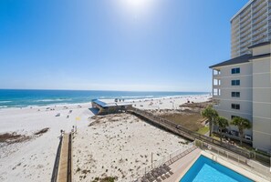 A beach view from a hotel with a pool, a boardwalk, and a beach area.