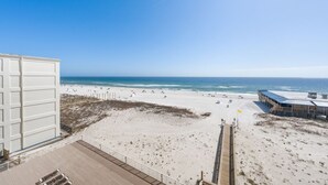 Blick auf einen Strand von einem Gebäude mit einer Holzterrasse und einem Sandstrand im Vordergrund.