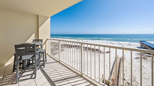Ein Balkon mit Blick auf den Strand, einem Geländer und einem Tisch mit Stühlen.