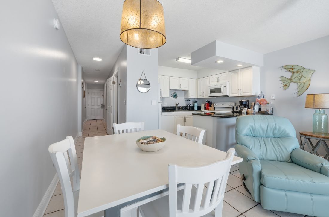 A modern kitchen with white cabinets, a dining table with chairs, a light blue sofa, and a pendant light.