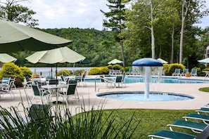 A pool area with lounge chairs and umbrellas, surrounded by greenery and trees.