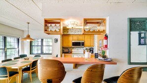 A modern kitchen with wooden cabinets, a central island, and a dining area with wooden chairs.