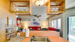 A compact kitchen with a sink, a ceiling fan, and a dining area with a red sofa.