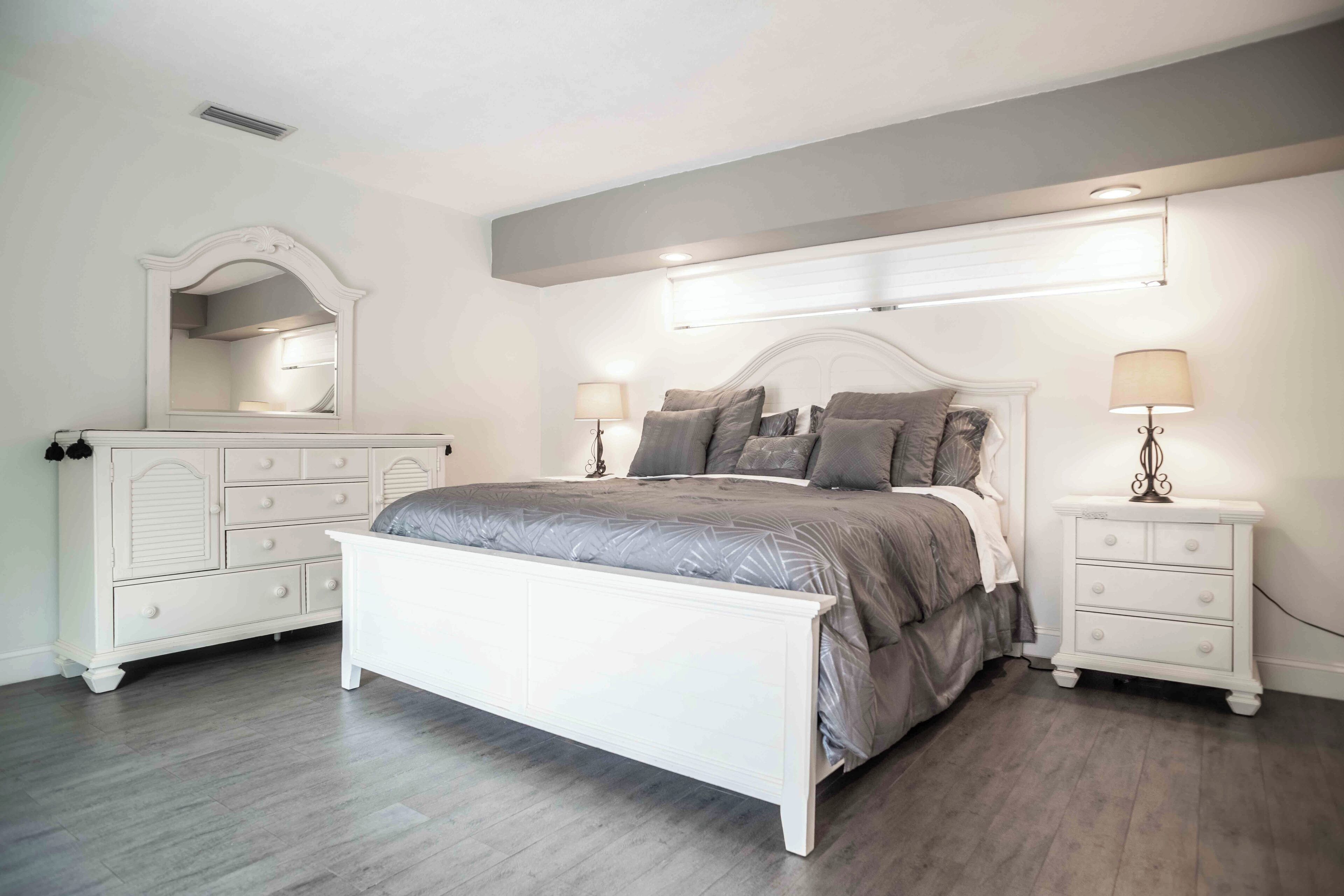 Une chambre avec un lit blanc, deux tables de chevet avec des lampes, une commode et un grand miroir.
