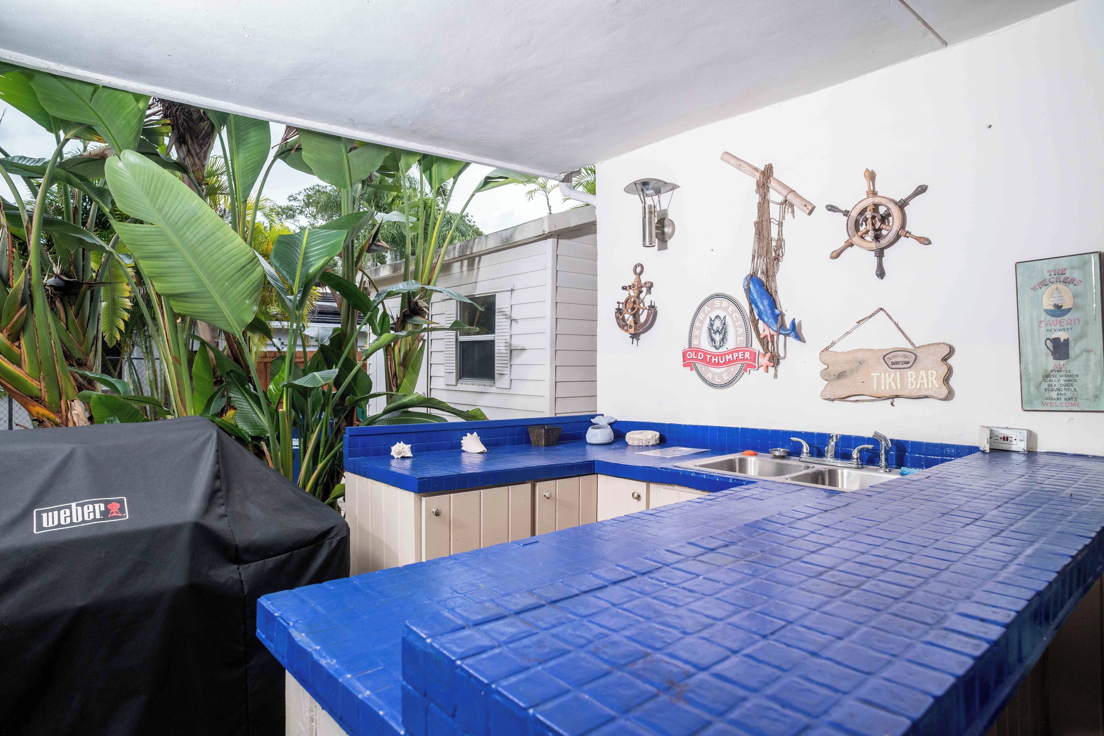 A kitchen with blue countertops, a Weber grill, and nautical-themed wall decorations.