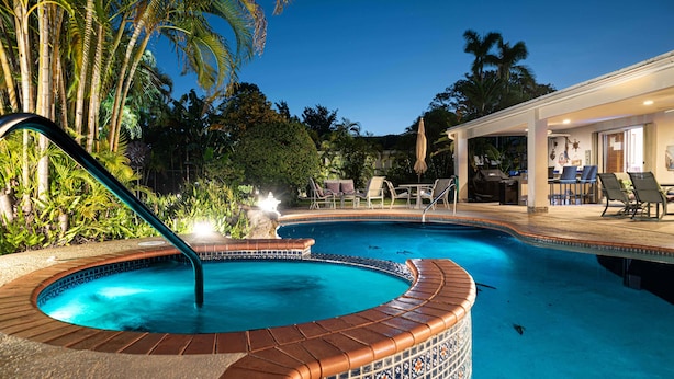 A swimming pool with a tiled edge, surrounded by lounge chairs and a covered patio area.