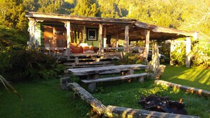 Una cabana rústica amb un porxo, bancs de fusta i una petita zona de jardí.