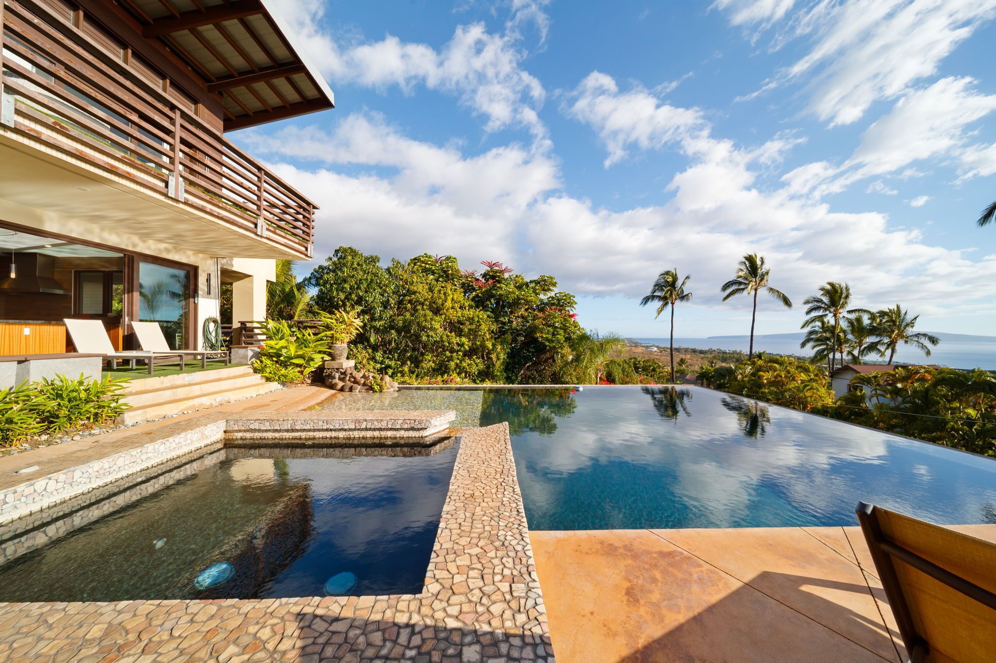 A modern house with a large infinity pool, a wooden deck, and a view of the ocean.
