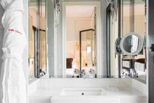 A modern bathroom with a large mirror, a white sink, and a robe hanging on the wall.