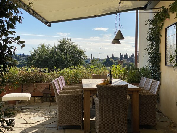 A covered patio with wicker furniture, a table with a bottle and glass, and a view of a cityscape. - Renovated gorgeous villa in Florence. Walking distance to all sites. (Firenze)