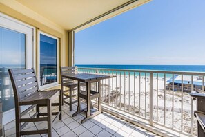 Un balcon avec une table et des chaises, donnant sur une plage et offrant une vue dégagée sur l’océan.