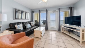 Een woonkamer met een zwarte leren bank, een houten salontafel, een televisie op een houten dressoir en een plafondventilator.