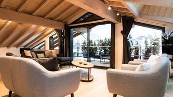 A spacious loft with high ceilings, wooden beams, and large windows offering a view of a snowy landscape.