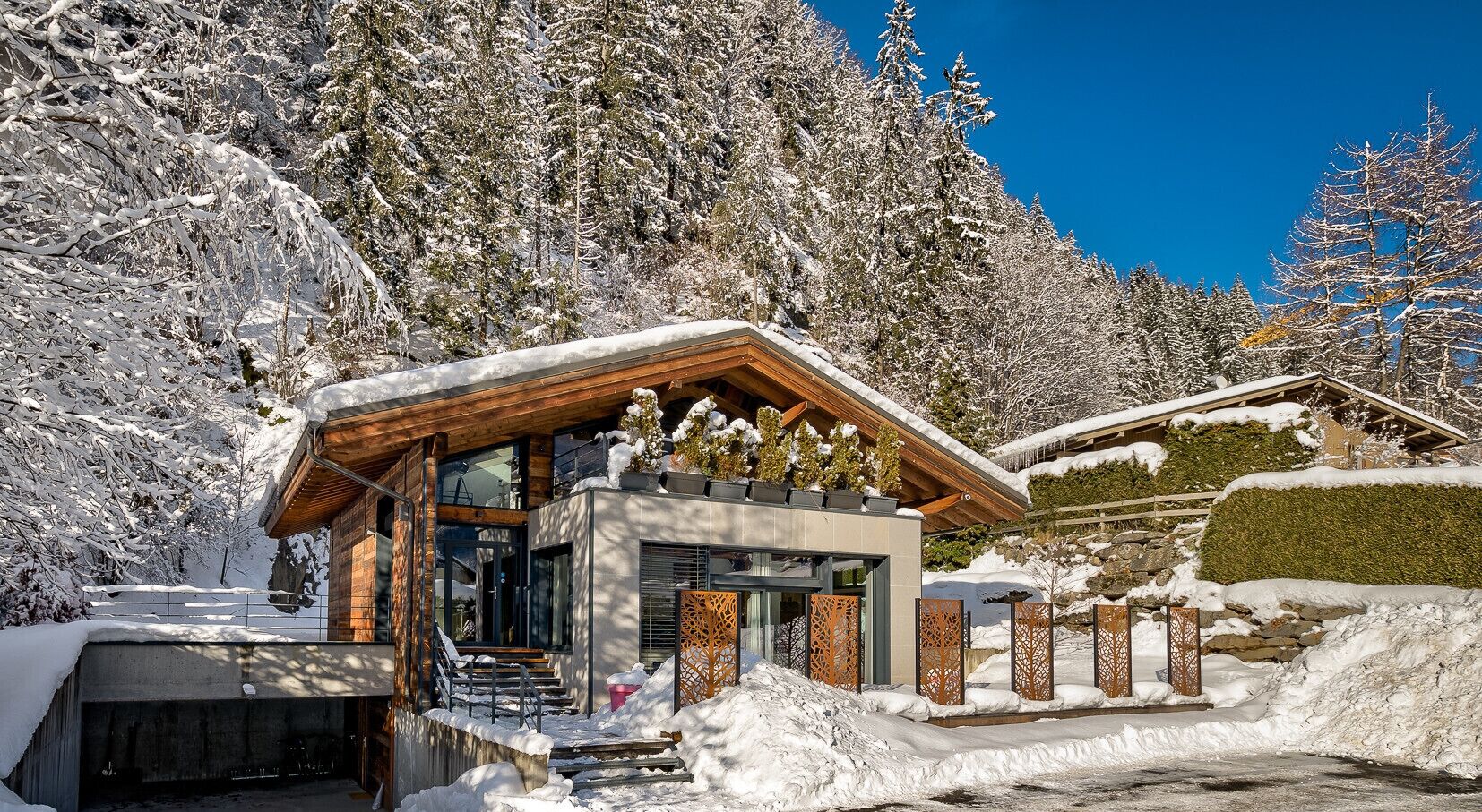 Un chalet moderne avec une façade en bois, une entrée en verre et un paysage enneigé.