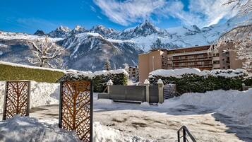 A snow-covered courtyard with a mountain backdrop, a building with balconies, and a wooden fence.