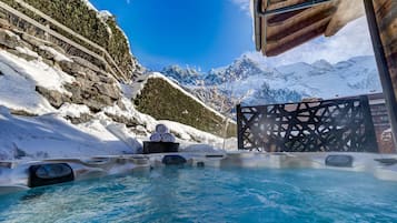 A hot tub with a view of snow-covered mountains and a wooden structure.