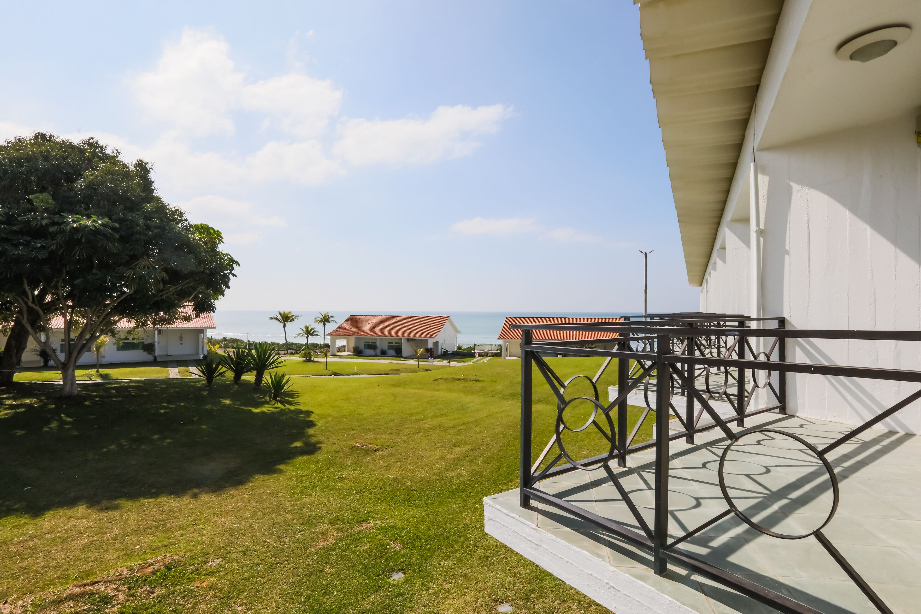 Uma varanda com guarda-corrimão de metal, com vista para uma área gramada e uma casa ao fundo.
