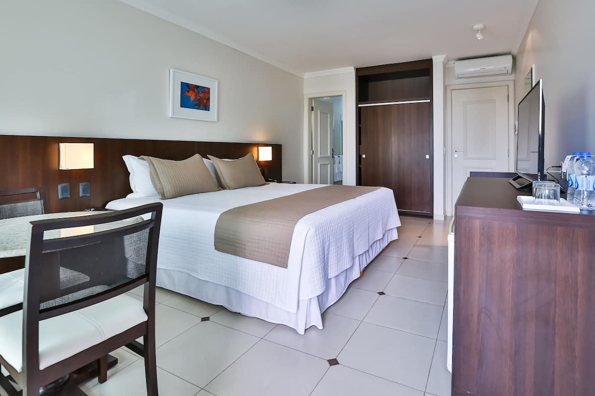 A hotel room with a bed, bedside table, chair, desk, and wardrobe.